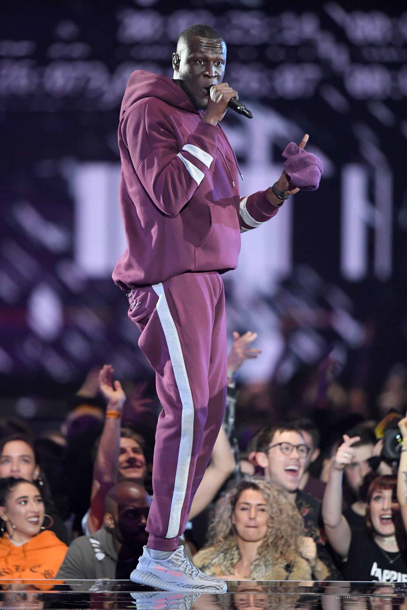 Stormzy wore the Beluga 2.0 early, and adidas’s VP called them 100% real. Stormzy full length on the EMAs stage in a maroon tracksuit and Beluga 2.0, crowd below, SSE Arena, Wembley, 12 Nov 2017.