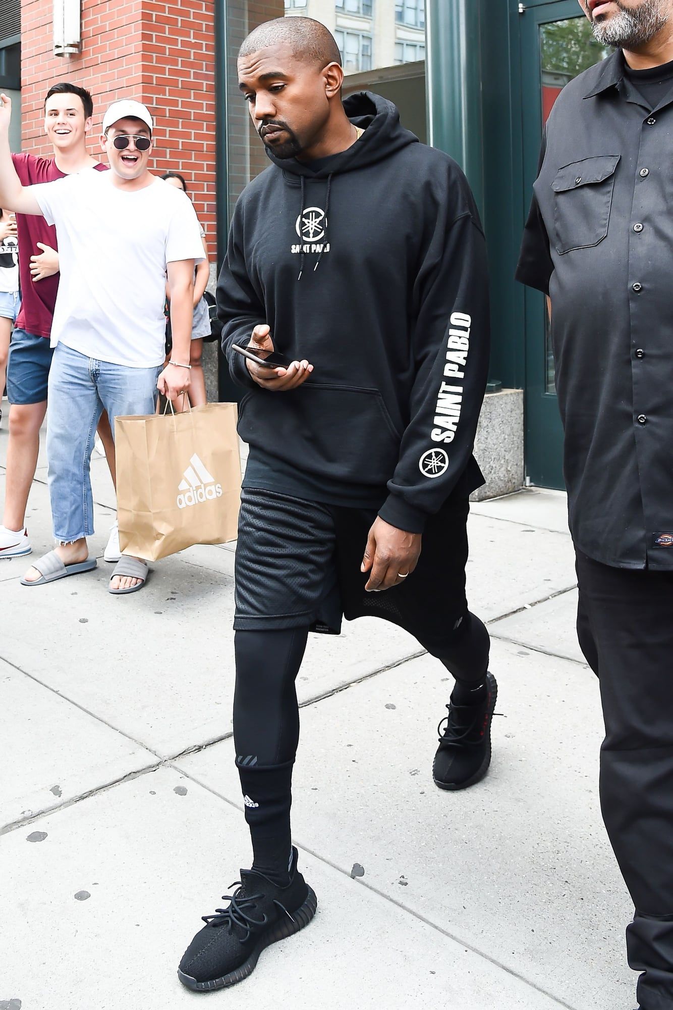 Ye’s Saint Pablo Tour had no stage, just a platform floating over the crowd. Ye on the street in New York, 26 Aug 2016, the day after the Indianapolis opener: black Saint Pablo hoodie, mesh shorts over leggings, black 350 V2s with SPLY-350 in red.