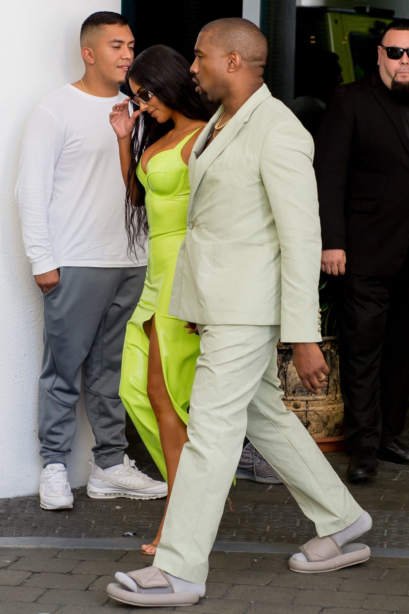 Ye posted the first Yeezy Slide in 2018 and called it a rough draft. Ye in a mint Louis Vuitton suit and the in-house Yeezy slides, heels over the back, arriving with Kim Kardashian at 2 Chainz's wedding, Miami, Aug 2018.