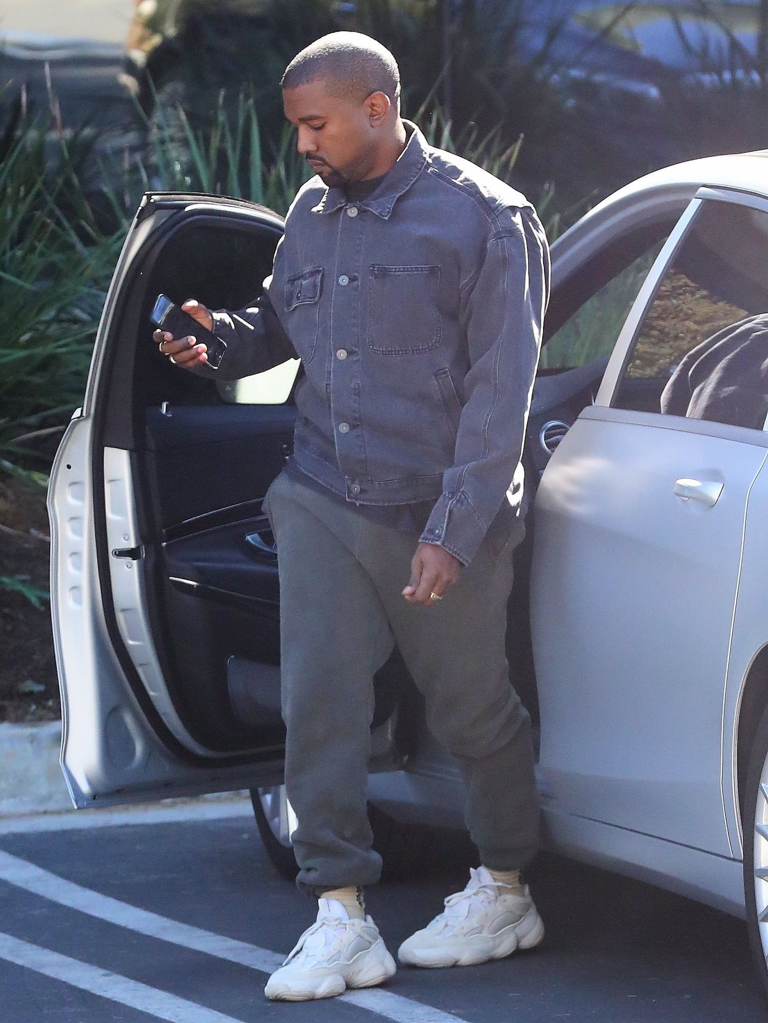 The Yeezy 500 went from nameless sample to infant sizes in under seven years. Ye in a pale pre-release Yeezy 500, denim jacket and grey sweatpants, stepping out of a car, late 2017.