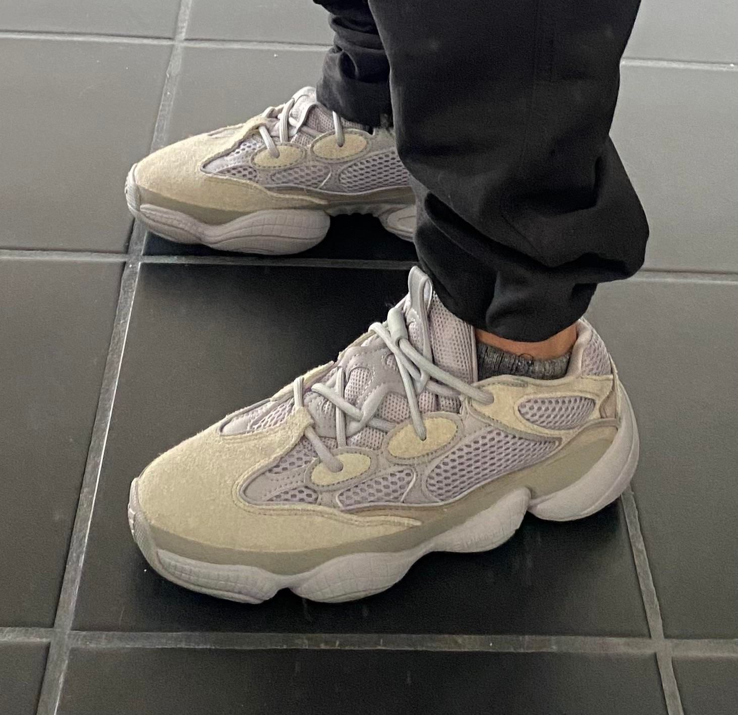 The Yeezy 500 went from nameless sample to infant sizes in under seven years. Yeezy 500 Stone Salt on foot, black joggers, dark tiled floor.