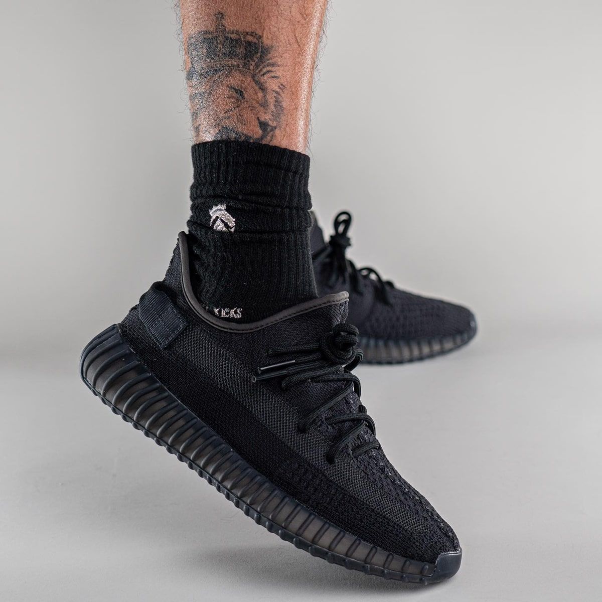 The black 350 V2 lost a little more of its stripe every time. Onyx on foot, black socks, grey studio floor, Feb 2022.
